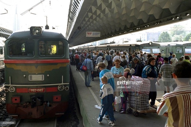 Überfüllter russischer Bahnhof in St. Petersburg (ehemals Leningrad). Zugreisende warten mit ihrem Gepäck auf dem überdachten Bahnsteig, an dem zu beiden Seiten Züge halten (October 21, 1999).jpg